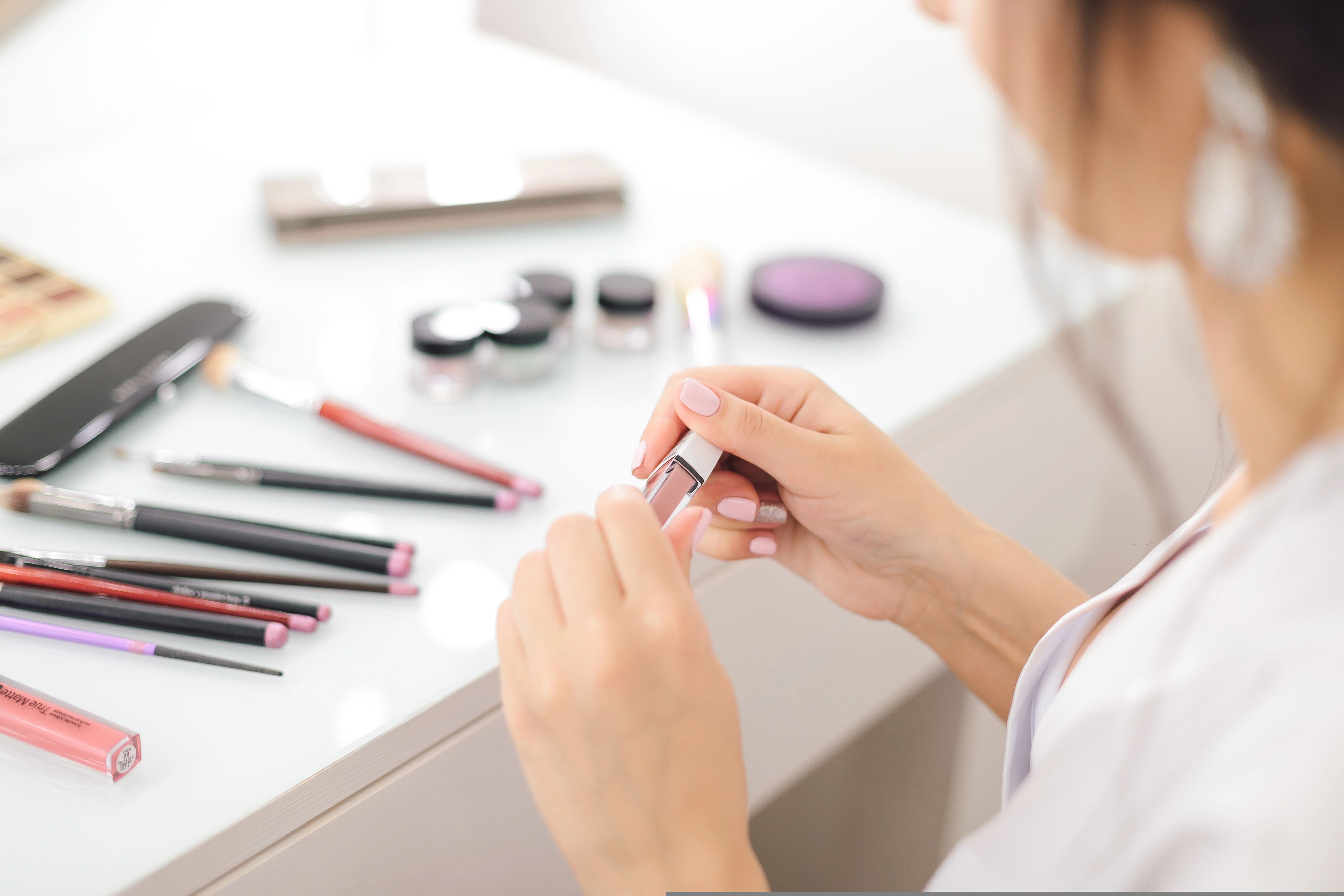Shopper opening a lipstick tester beside makeup brushes and color products